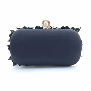 Detailed view of black evening clutch bag with sequin flower trim and pearl clasp.