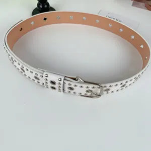 Nahaufnahme eines weißen Punk Ledergürtels mit vielen Metallösen und silberner Schnalle Detail.