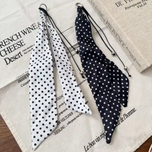 Dettaglio sciarpa lunga in seta a pois neri e bianchi, cintura a nastro in vita versatile.