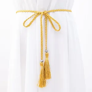 Close up view of a yellow braided tassel waist belt with rhinestone details on white dress.