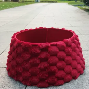 Vue détaillée en extérieur d'une jupe de sapin de Noël en peluche rouge avec motif 3D texturé unique.