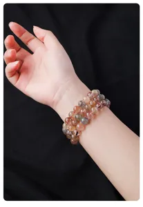 Close-up detail of natural multi-color rutilated quartz crystal bead bracelet on wrist.