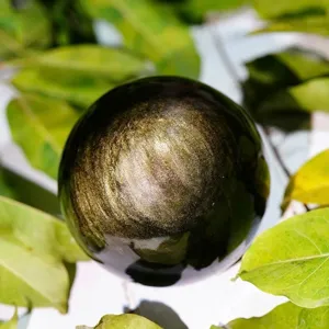Close-up shot of natural golden obsidian crystal sphere featuring stunning gold sheen effect.