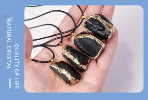 Close-up detail of natural black tourmaline raw stone pendant with gold edge and black cord.