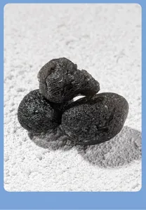 Natural black tektite rough stone detail view, raw meteorite mineral specimen closeup.