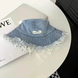 Washed denim bucket hat with distressed frayed edges and metallic brand tag detail.