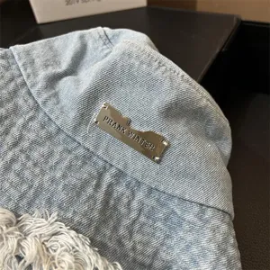 Detailed view of washed denim bucket hat with metal brand tag and frayed brim, spring sun hat.