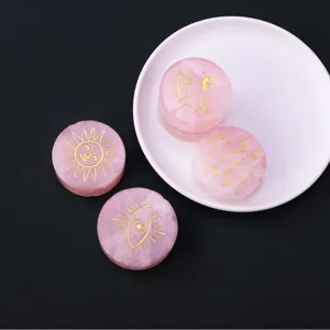 Natural rose quartz crystal disc with gold engraved mystical sun and moon symbols detail.
