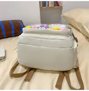 Detailed view of white canvas backpack with transparent front pocket and colorful pom poms.