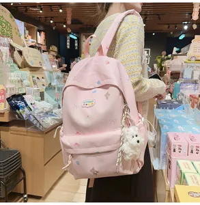Cute pink student schoolbag with bear print and fluffy plush pendant, detail view of backpack.