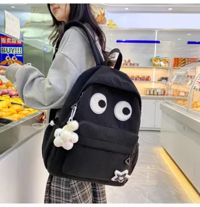 Black corduroy backpack detail featuring funny eye patches and cute plush flower pendant.