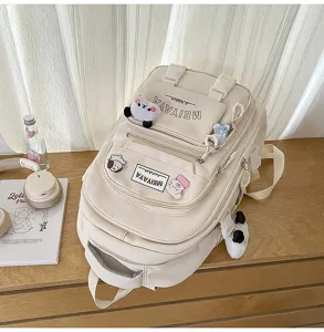 Detail view of cream canvas school backpack with multiple pockets, cute charms and sturdy straps.