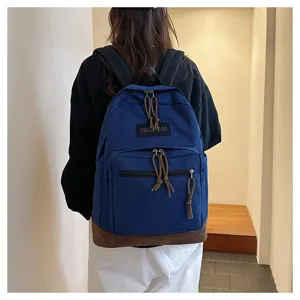 Detail view of casual canvas backpack with brown bottom, front zip pocket, and straps.
