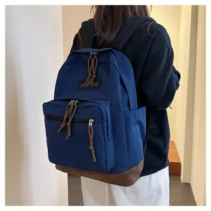 Detailed view of casual blue backpack with brown leather bottom and front zipper pocket.