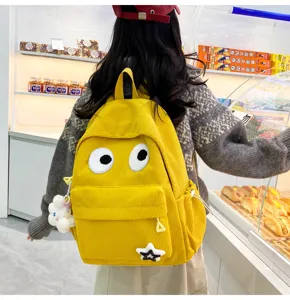 Detail view of yellow corduroy backpack with cute big eyes and lovely charms for students.