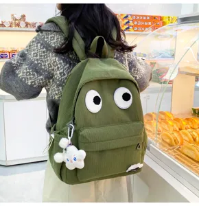 Detail view of cute green corduroy backpack with big eyes and fluffy pendant for students.