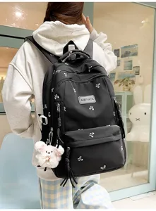 Detailed view of black student backpack with white bow prints, front pocket and cute pendant.
