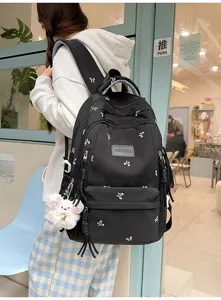 Detailed view of casual black backpack with cute bow prints and plush bear pendant.