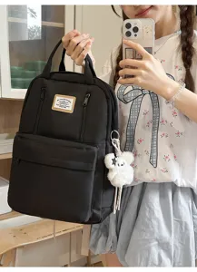 Detailed view of a casual black backpack with front zipper pockets, label patch, and cute bear charm.