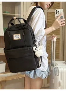 Detail view of black casual school backpack with front zipper pocket and cute plush pendant.