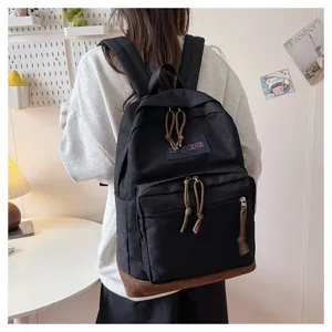 Detail view of casual black student backpack with brown bottom and convenient zipper compartments.