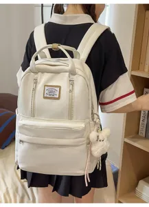 Detailed shot of white casual backpack worn on back, featuring multiple pockets and furry keychain.