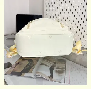 Detail view of cute white backpack with bow embroidery and yellow straps in daily scene.