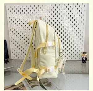 Side detail view of a cute light yellow canvas backpack with embroidered bow patterns and straps.