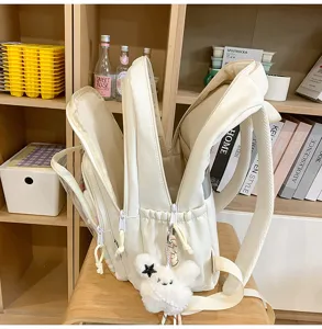 Detalle de la mochila escolar crema con múltiples bolsillos y colgante de conejito.