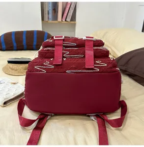 Dark red school backpack detail with crinkled fabric, pink straps, and white wave stitching.