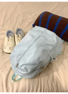 Detail view of light blue backpack featuring cute bow embroidery and zipper closure.
