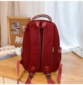 Detailed view of the red backpack showing back straps and zipper pocket design on wooden desk.