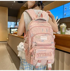 Pink quilted student backpack detail showing embroidered patterns, patch labels and cute plush pendant.