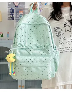 Detail shot of mint green polka dot backpack with cute bows and plush pendant in lifestyle room.