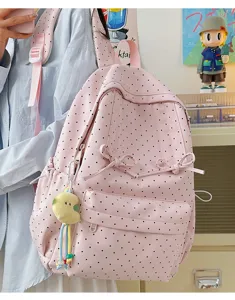 Pink polka dot backpack detail showing cute bow accents, front pocket, and plush pendant.