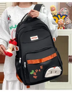 Mochila escolar negra de nailon con colgante de manzana y gran compartimento para viajes y estudios.