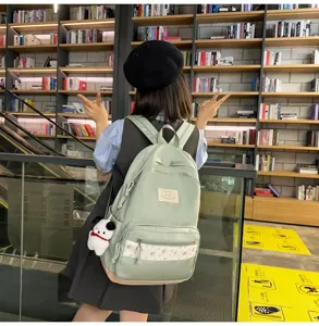 Casual green school backpack with floral front pocket and cute plush pendant for daily commute.