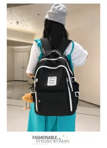 Detail view of stylish black canvas backpack with white contrast piping and cute plush charm.
