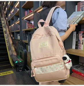 Detailed view of the pink student school backpack featuring floral patchwork and cute plush pendant.