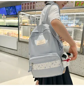 Detail view of a light blue canvas school backpack with floral patch and cute plush dog pendant.
