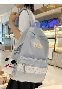 Close-up of light blue student backpack with floral patch and cute puppy charm detail.