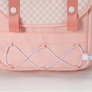Dettaglio zaino rosa con patta a quadretti, cinghie bianche e cordino elastico.