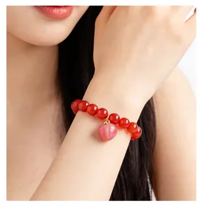 Natural red agate bead bracelet with a cute pink peach heart charm on wrist view.