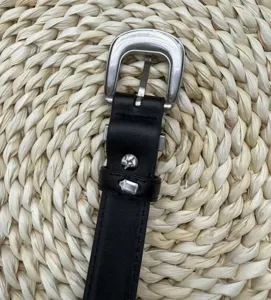 Close up detail shot of black leather belt with silver buckle and vintage engraved metal rivets.