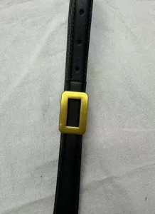 Close up detail of black leather slim belt with a luxury gold rectangular buckle.