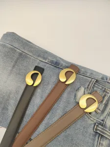 Close-up of women's thin leather belts with unique gold metal buckles in black, brown, and grey.
