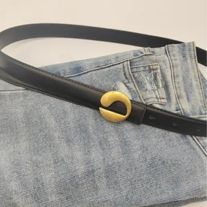 Black leather belt for women with modern gold metal buckle over stylish denim jeans.