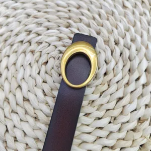 Close-up detail van een donkerbruine echt lederen damesriem met vintage gouden ovale gesp.