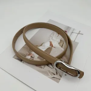 Gros plan détaillé de la fine ceinture en cuir beige minimaliste avec boucle argentée.