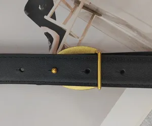 Gros plan détaillé de la ceinture en cuir noir avec une élégante boucle ovale dorée.
